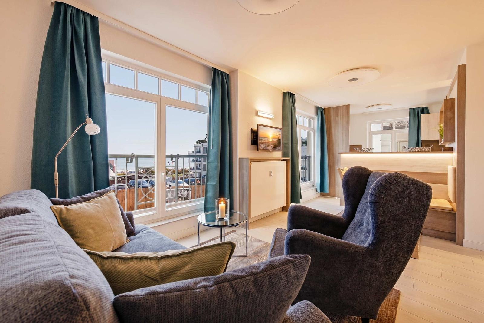 Wohnbereich mit Sofa, Sessel und Blick auf Balkon mit Meerblick.