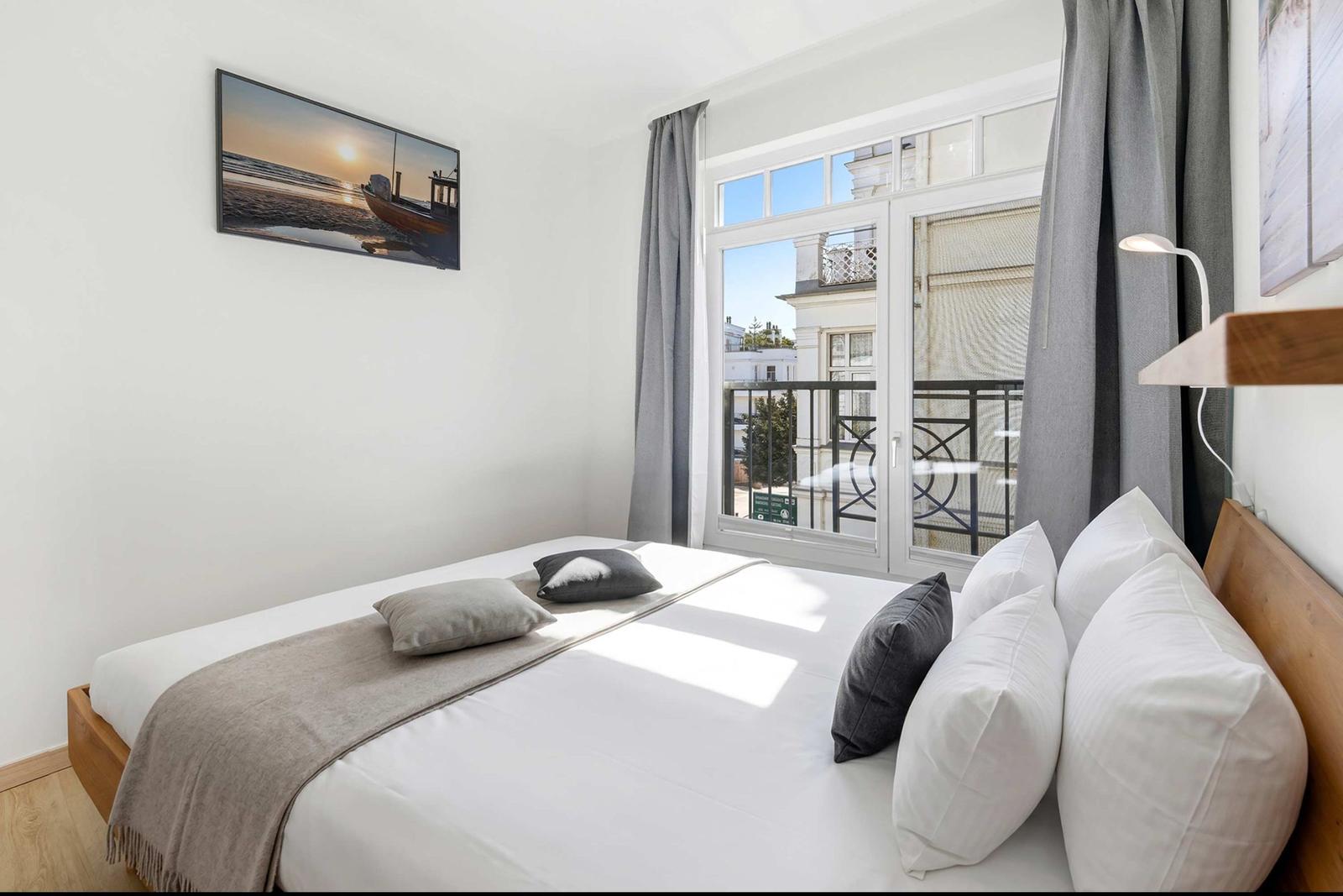 Ein Schlafzimmer mit Bett, Fenster und Balkon. Wandbild und graue Vorhänge.