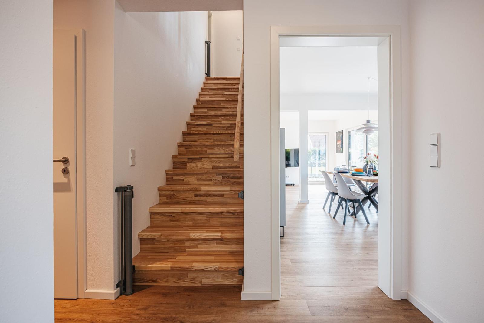 Haus mit Holztreppe und Blick in Esszimmer mit Tisch und Stühlen.