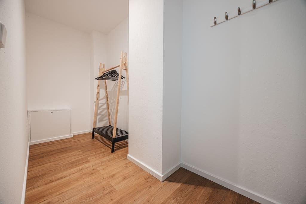 Ein kleiner Raum mit Holzboden, Kleiderständer und Wandschrank. An der Wand hängen Haken.