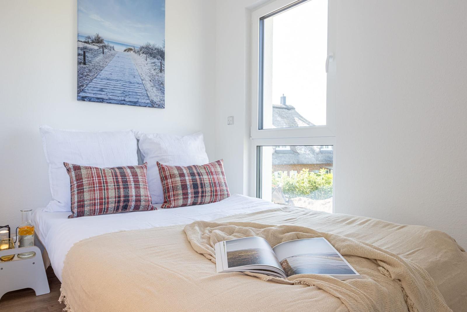 Schlafzimmer mit Bett, Kissen und Fensterblick auf Dach