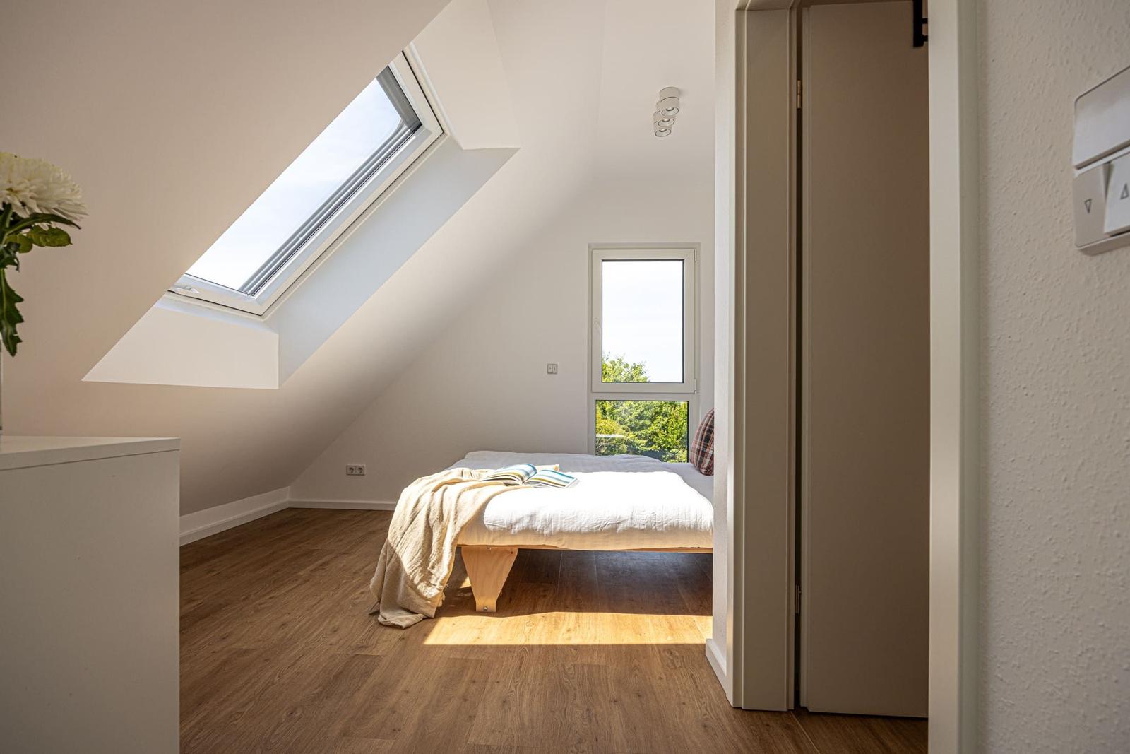 Schlafzimmer mit Dachschrägen, Dachfenster und Fenster mit Blick auf Grün.