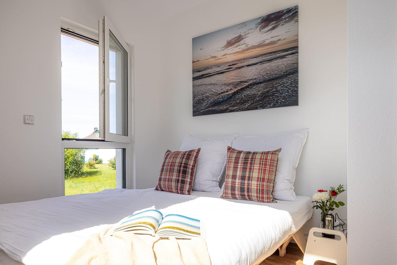 Schlafzimmer mit Blick auf grünes Gelände. Bett mit Kissen und Wandbild.