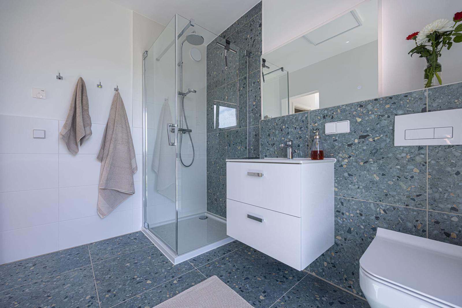 Badezimmer mit Dusche, Waschbecken und Toilette. Terrazzo-Fliesen und Spiegelschrank.