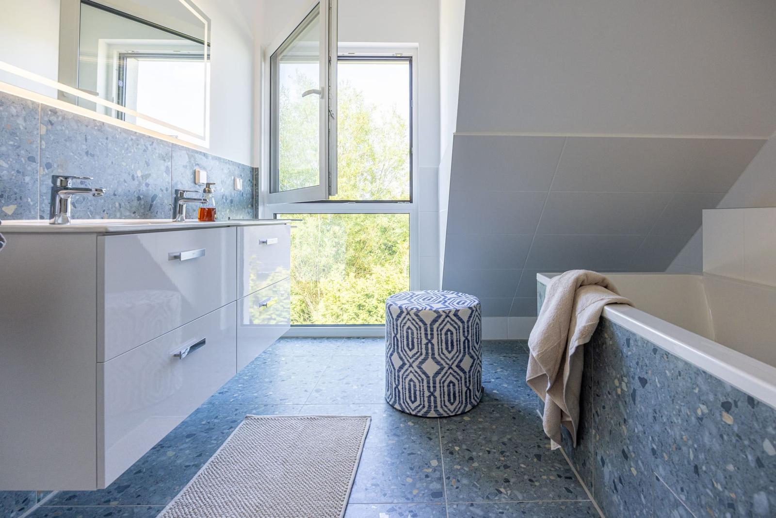 Badezimmer mit Waschbecken, Badewanne und Fenster zur grünen Aussicht.