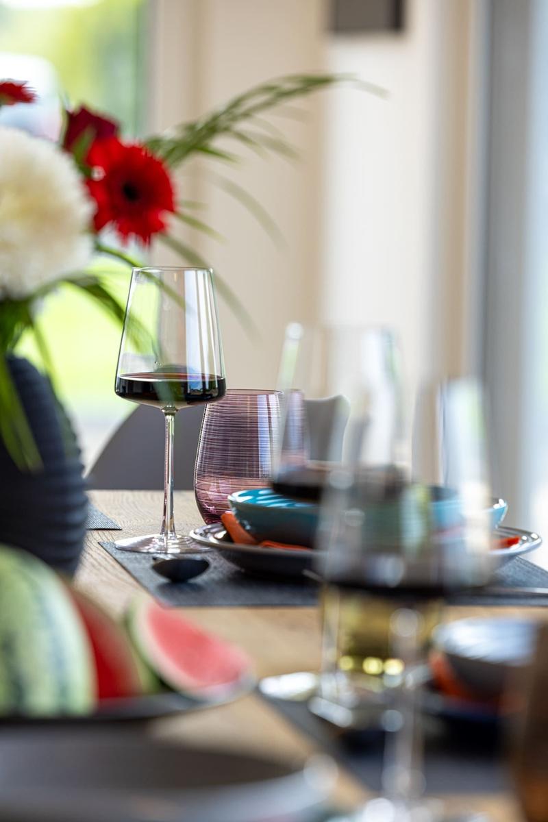 Tisch gedeckt mit Weinglas, Obst und Blumenarrangement.