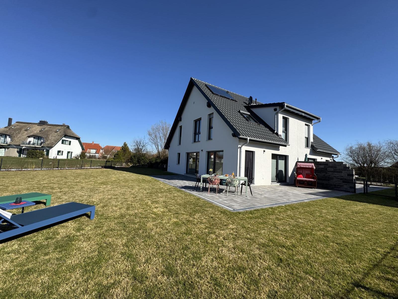 Modernes Haus mit großem Garten und Terrasse mit Gartenmöbeln und Liegestühlen.