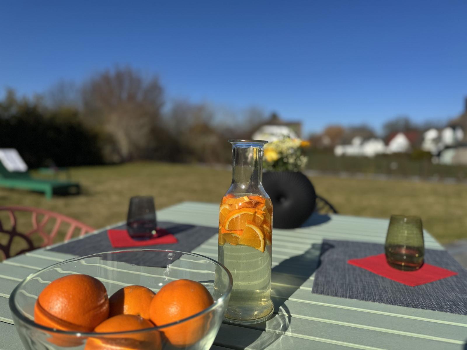 Außenbereich mit Tisch, Orangen und Orangensaft. Hintergrund: Grasfläche und Bäume.