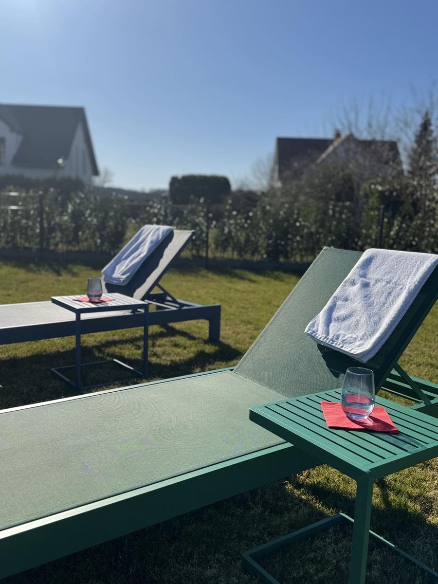 Zwei Liegestühle mit Tisch und Handtuch im Garten. Hintergrund: Hecke und Häuser.