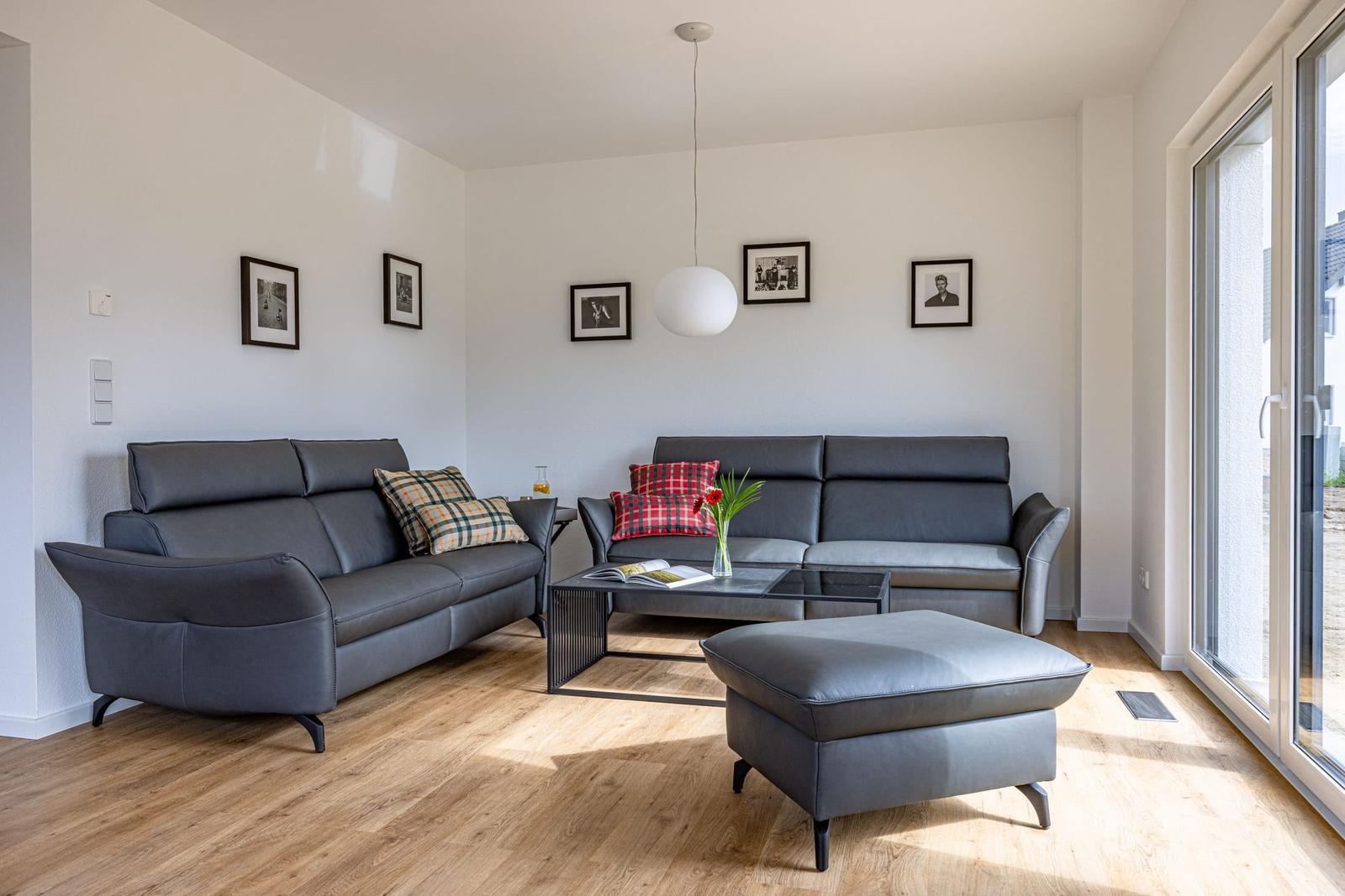 Zwei graue Sofas, ein Hocker und ein Tisch mit Blumen.
