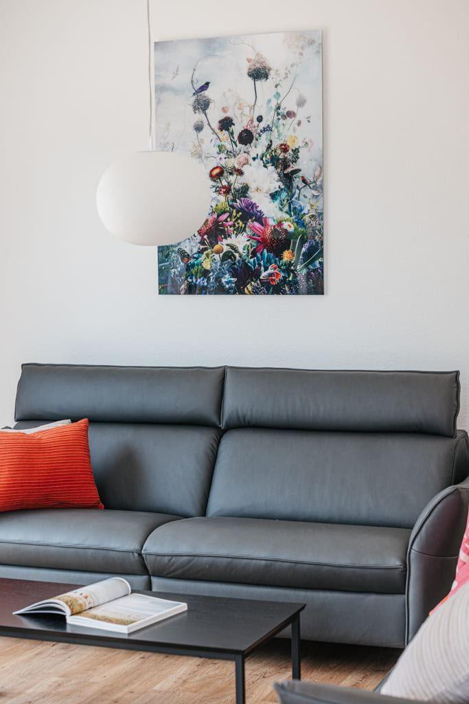 Graße Couch mit rotem Kissen, schwarzer Couchtisch und Wandbild mit Blumen.