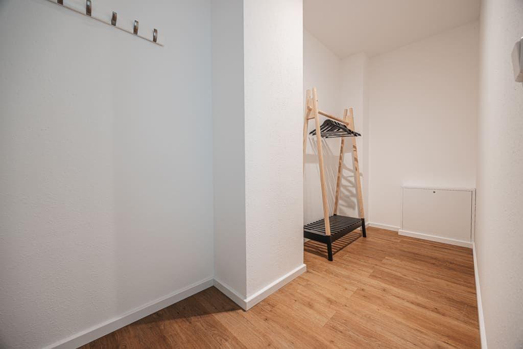 Kleiderständer und Haken an der Wand in einem Raum mit Holzboden.