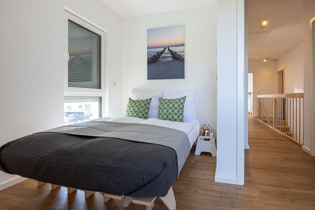 Schlafzimmer mit Bett, Fenster und Wandbild. Holzdielen und Sicht auf Flur.