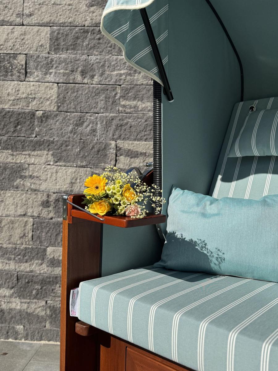 Hängesessel mit Streifenbezug und Blumen auf kleinem Tisch