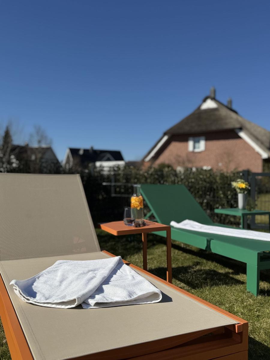 Terrasse mit Liegestühlen und Getränken. Hintergrund: Haus und Garten.
