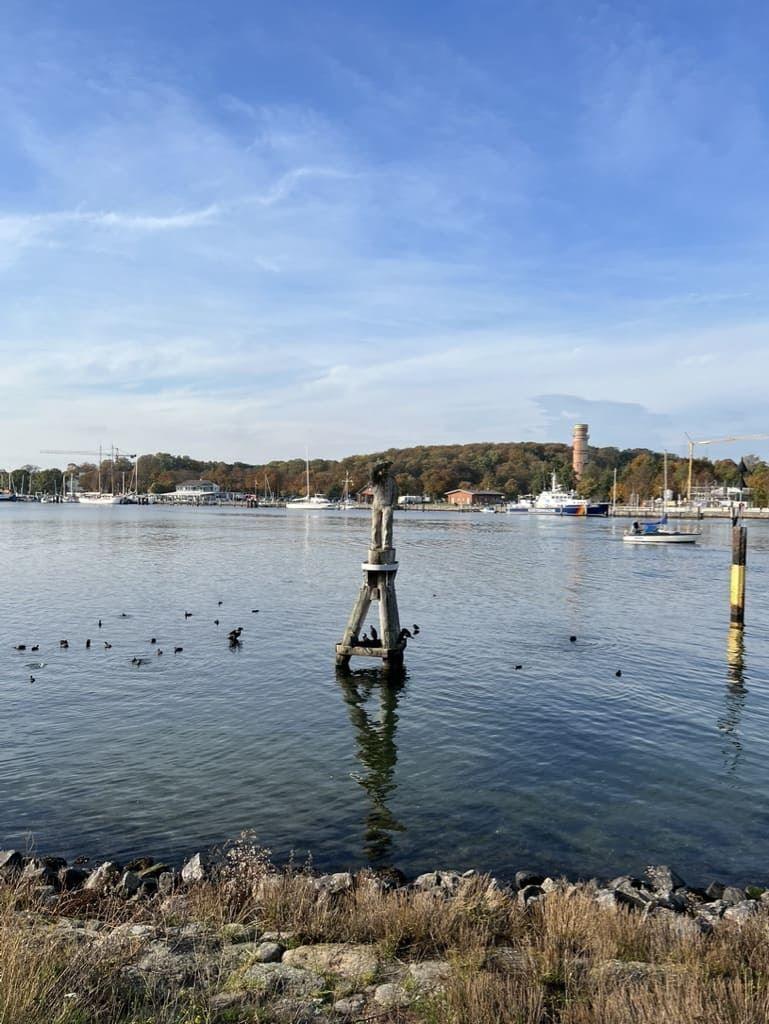 Wasserfront mit Steilufer, Booten und einem Turm im Hintergrund.