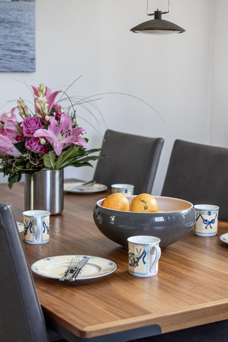 Esstisch mit Blumenvase, Obstschale und Tassen.