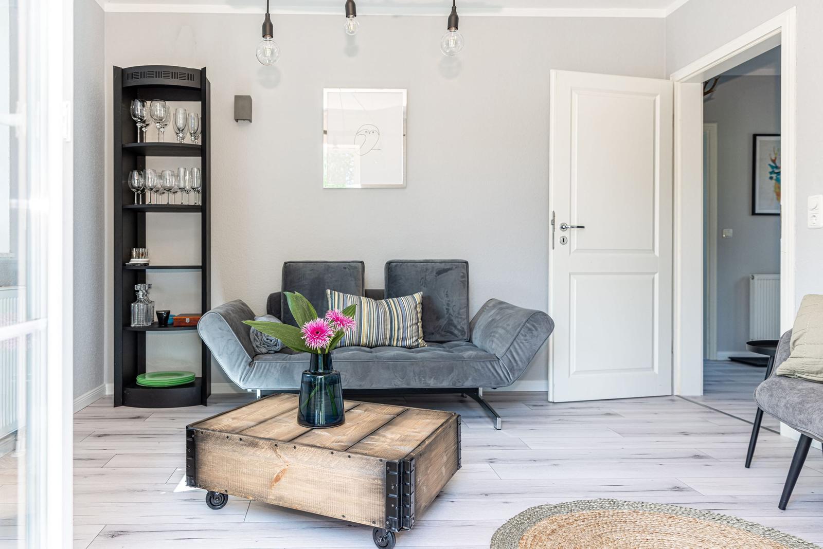 Ein Wohnzimmer mit grauem Sofa, Holztisch und Flur mit Tür.