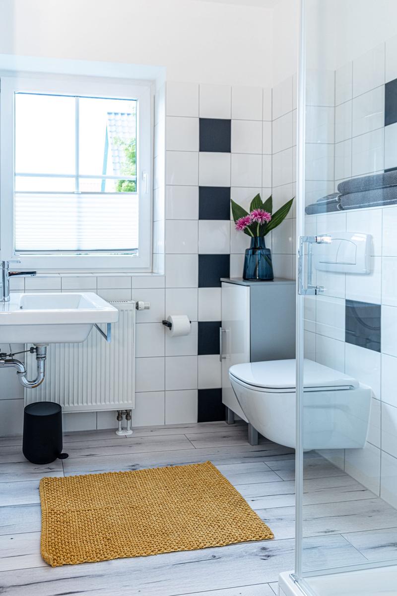 Badezimmer mit Waschbecken, Toilette und Dusche. Schwarze und weiße Fliesen. Gelber Teppich.