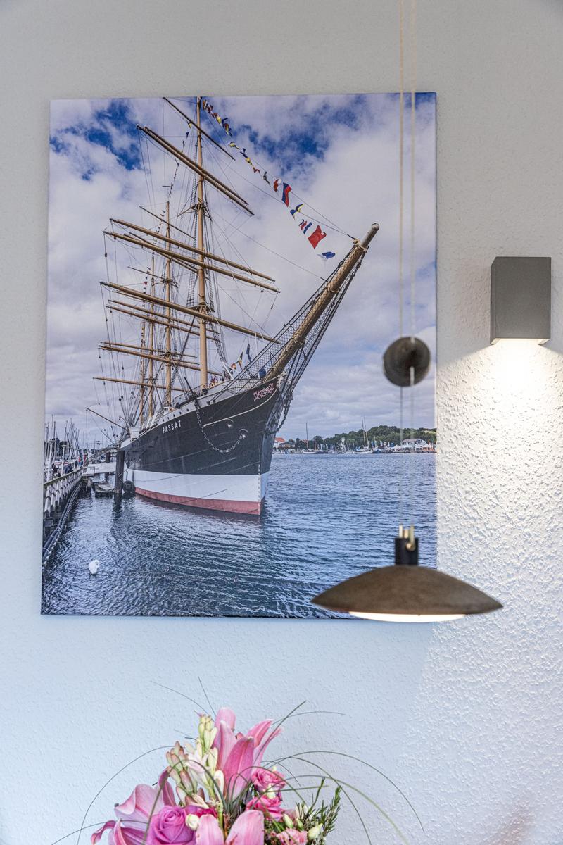Wandbild eines Segelschiffs am Hafen mit rosa Blumen und Deckenlampe.