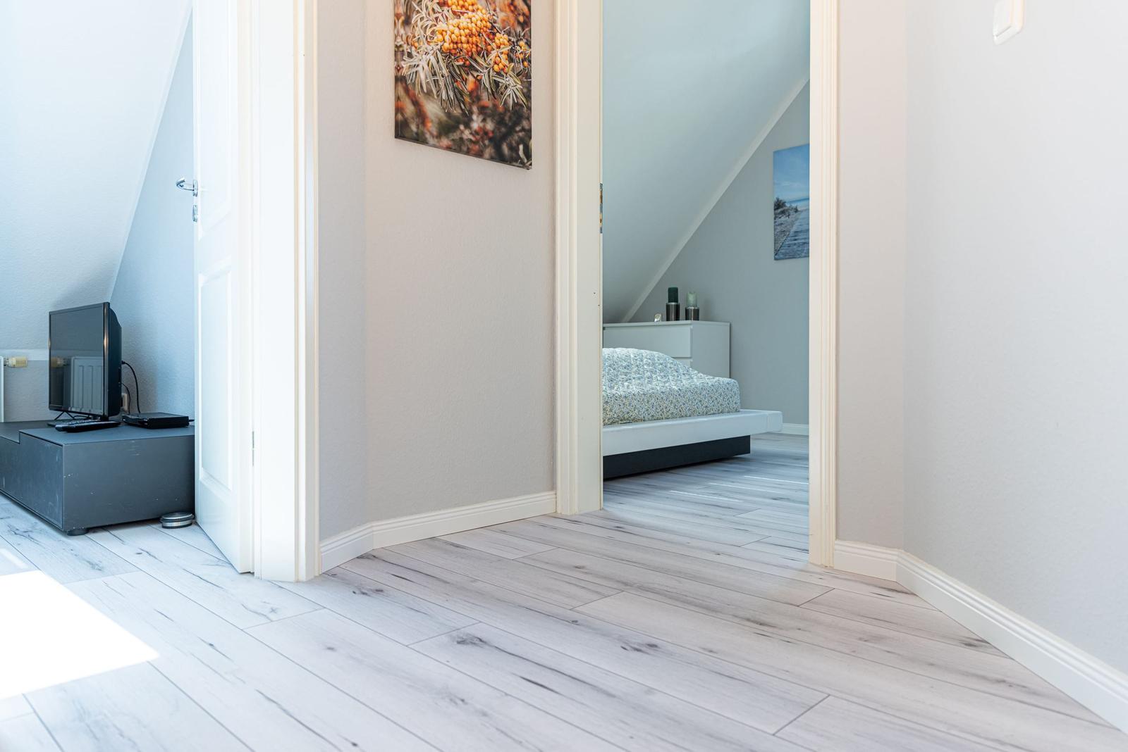 Flur mit Blick in Schlafzimmer und Wohnbereich mit Fernseher und Holzboden.