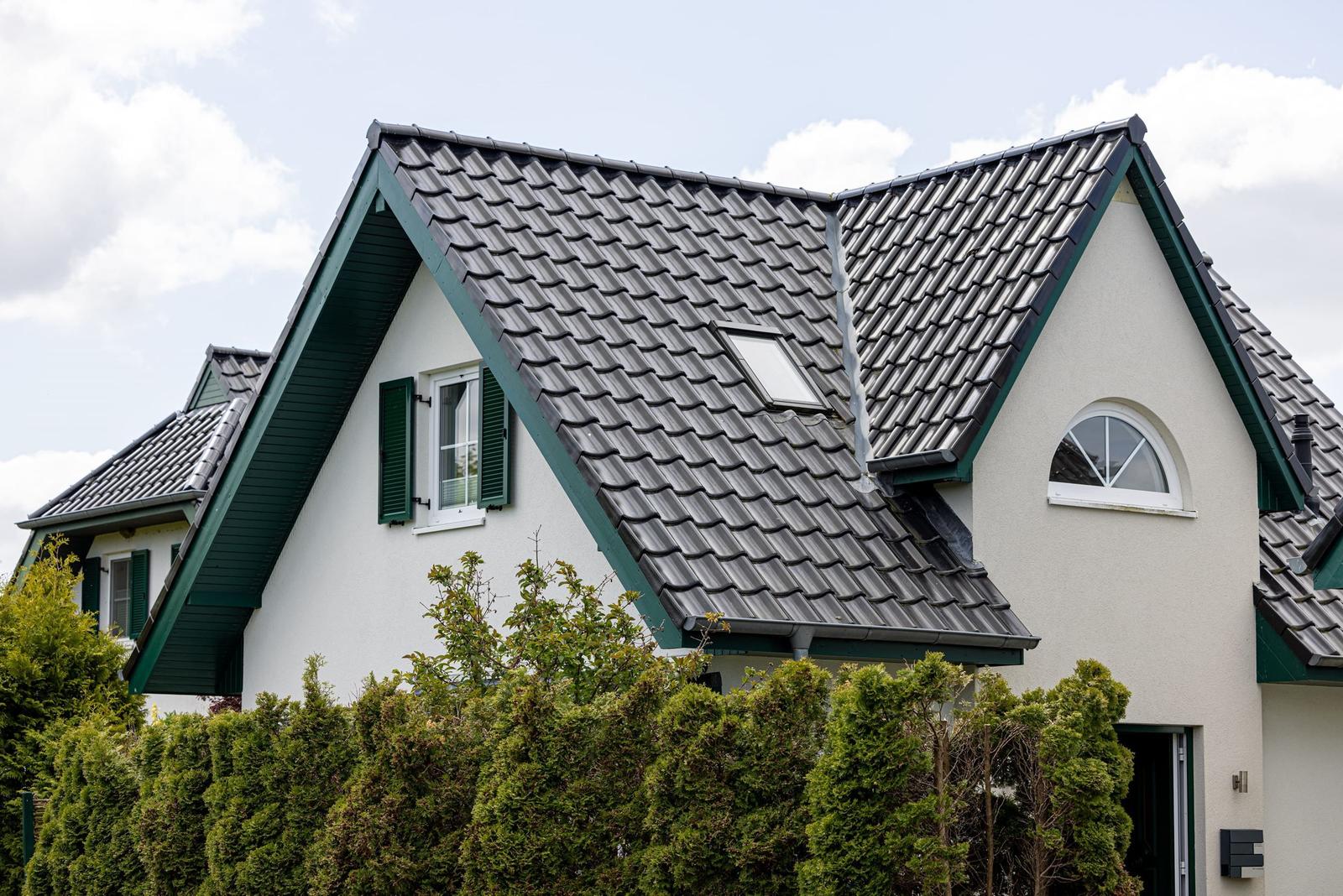 Haus mit grauem Dach und grünen Fensterläden, umgeben von grünen Hecken.