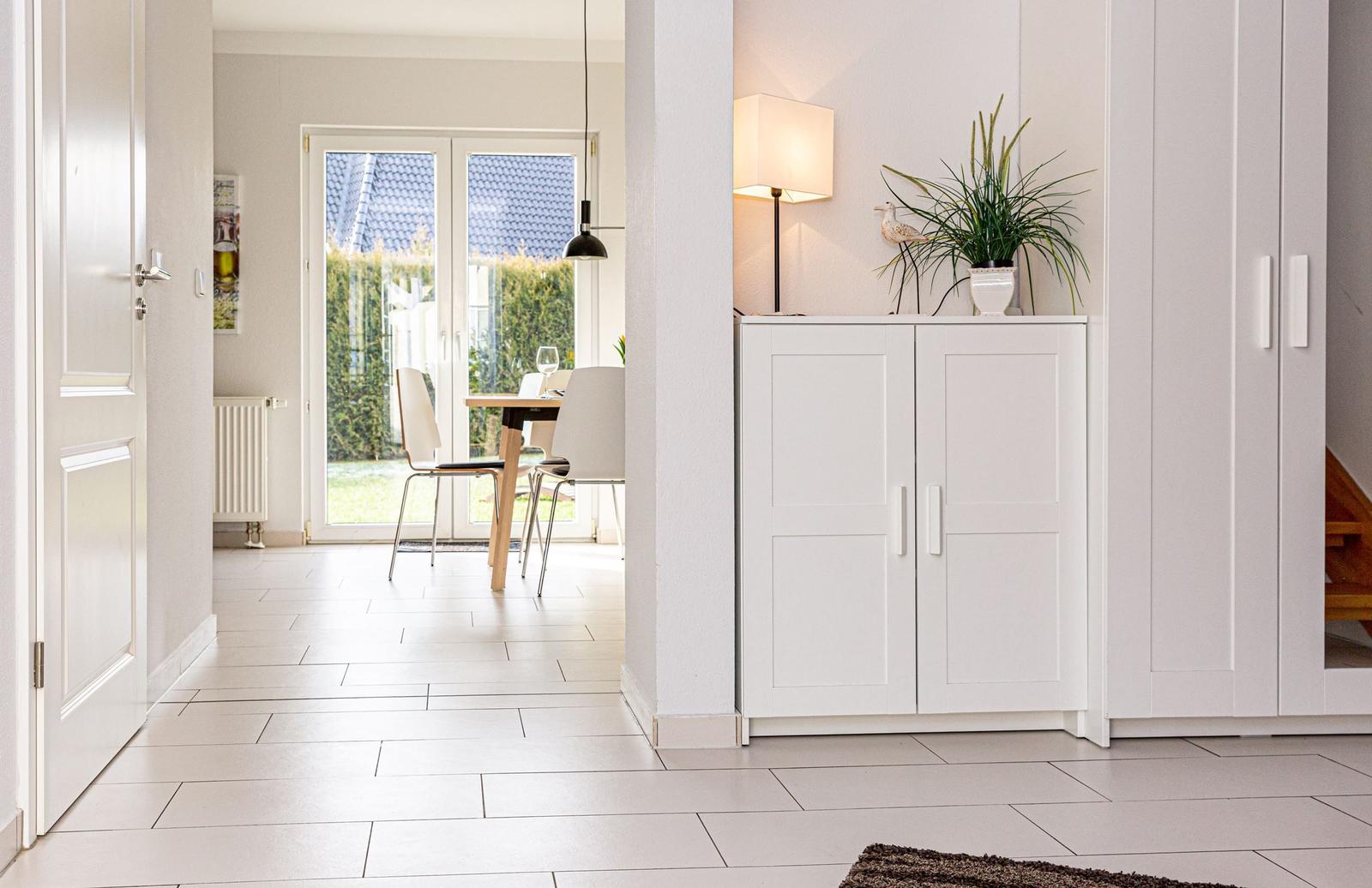 Haus mit weißem Schrank, Lampe und Pflanze. Durchgang zur Essnische mit Tisch und Stühlen.