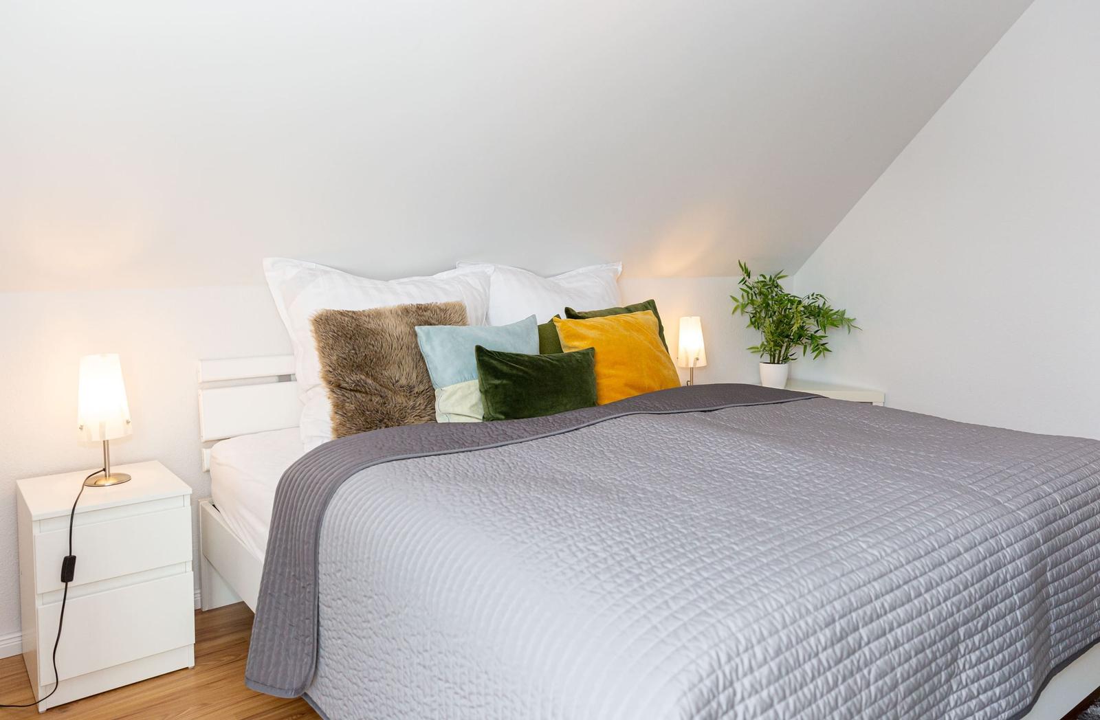 Schlafzimmer mit Bett, Kissen und Nachttischen unter schräger Decke.