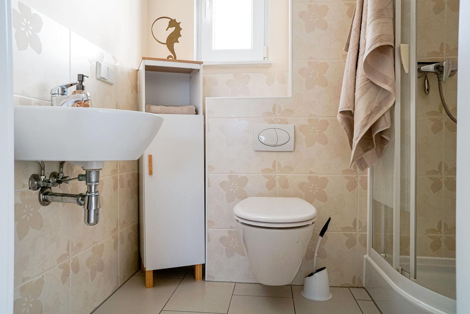 Badezimmer mit Waschbecken, Toilette und Dusche. Wandfliesen mit Blumenmuster.