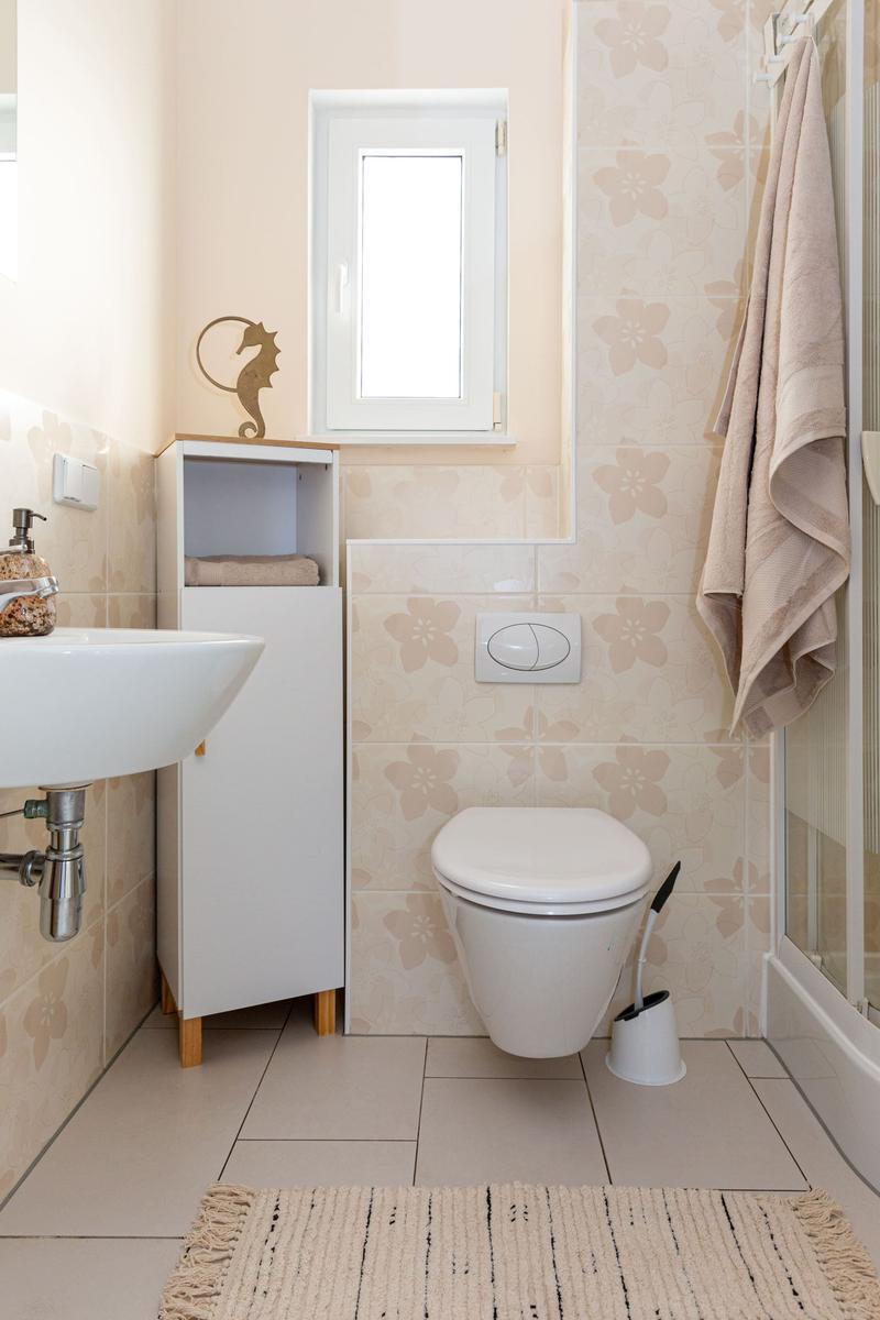 Badezimmer mit Waschbecken, Toilette, Dusche und Wandfliesen mit Blumenmuster.