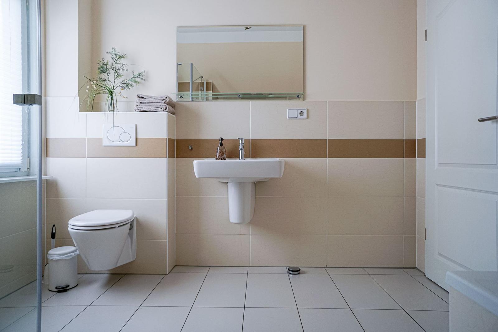 Badezimmer mit Waschbecken, Toilette und Spiegel. Wandgestaltung mit beige-braunen Streifen.