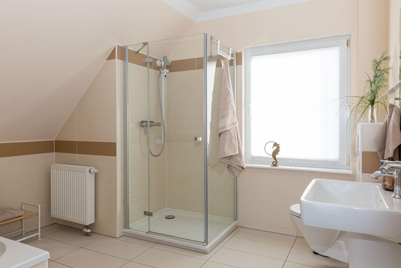 Badezimmer mit Dusche, Waschbecken und Toilette. Fenster mit Jalousie und Seepferdchen-Dekoration.