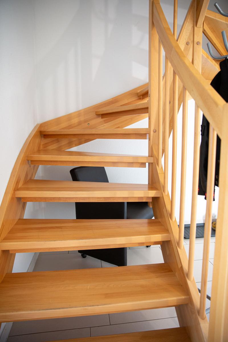 Holzgeländer und -treppe führen nach oben. Hinter der Treppe steht ein schwarzer Stuhl.