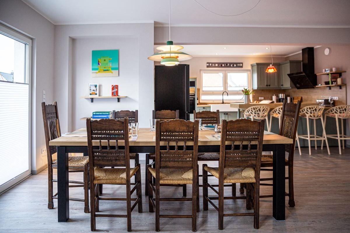 Esszimmer mit Holztisch und Stühlen, Küche im Hintergrund.