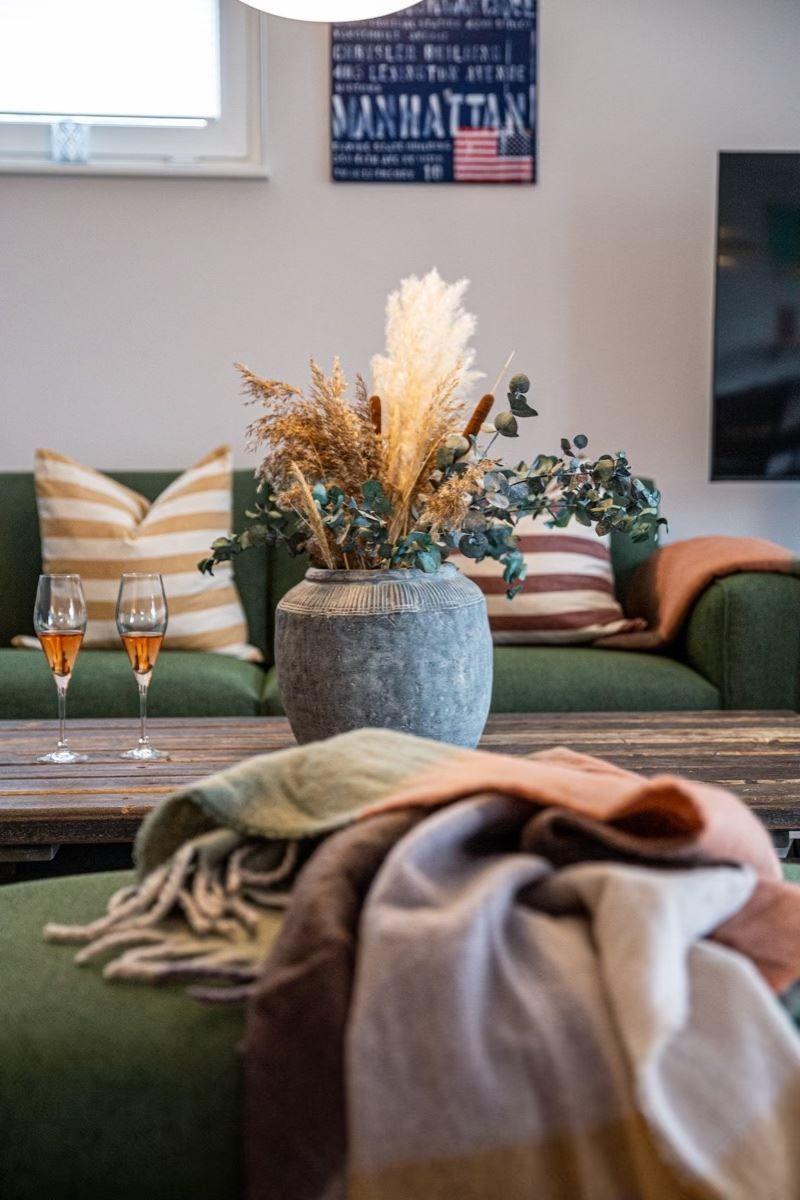 Ein Wohnzimmer mit grünem Sofa, Holztisch und Blumenarrangement.