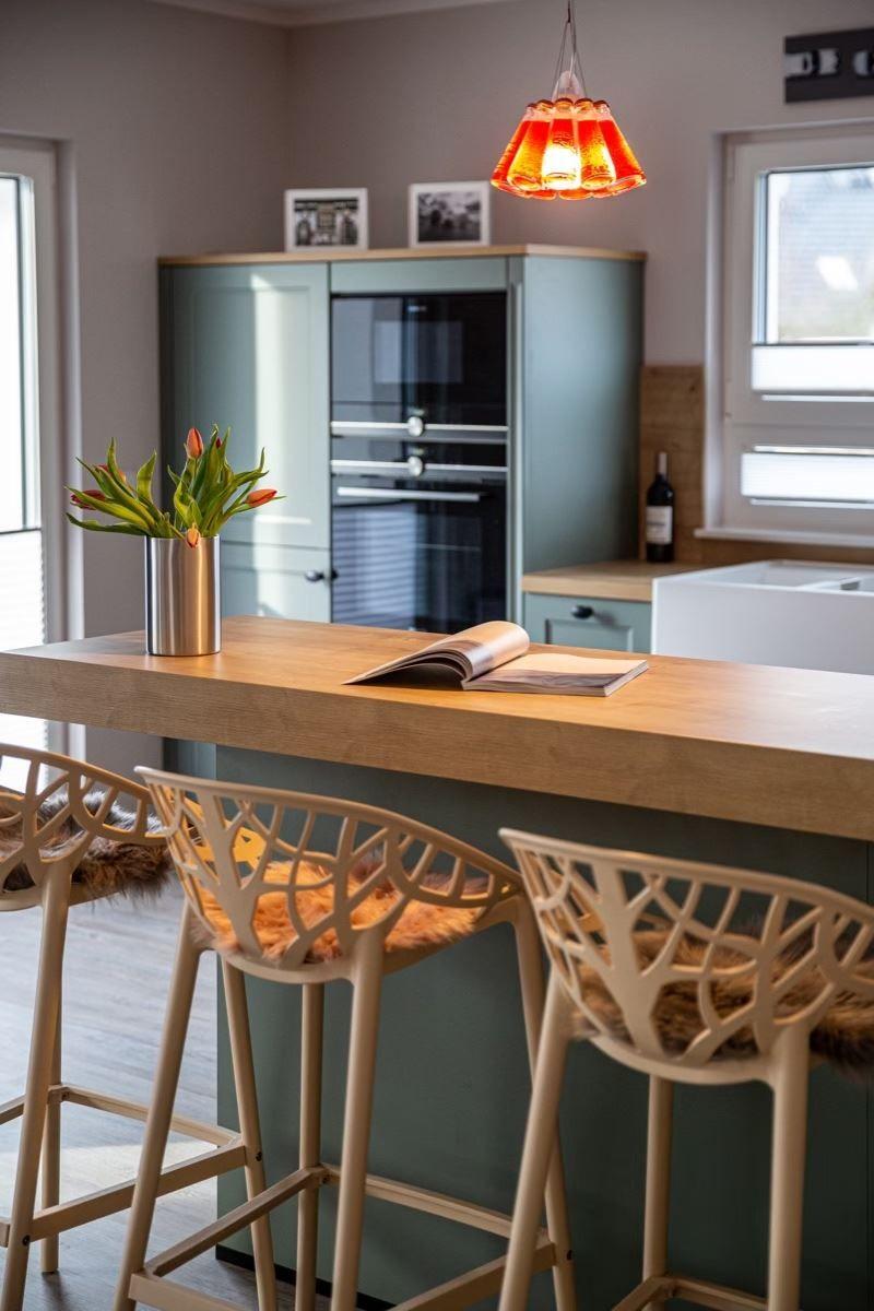Kücheninsel mit Holzoberfläche, drei Barhocker und einer Lampe darüber.