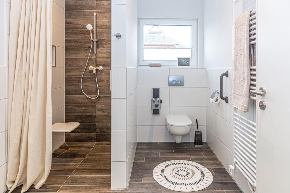 Badezimmer mit Dusche, Toilette und Heizkörper. Holzfliesen und Fenster.