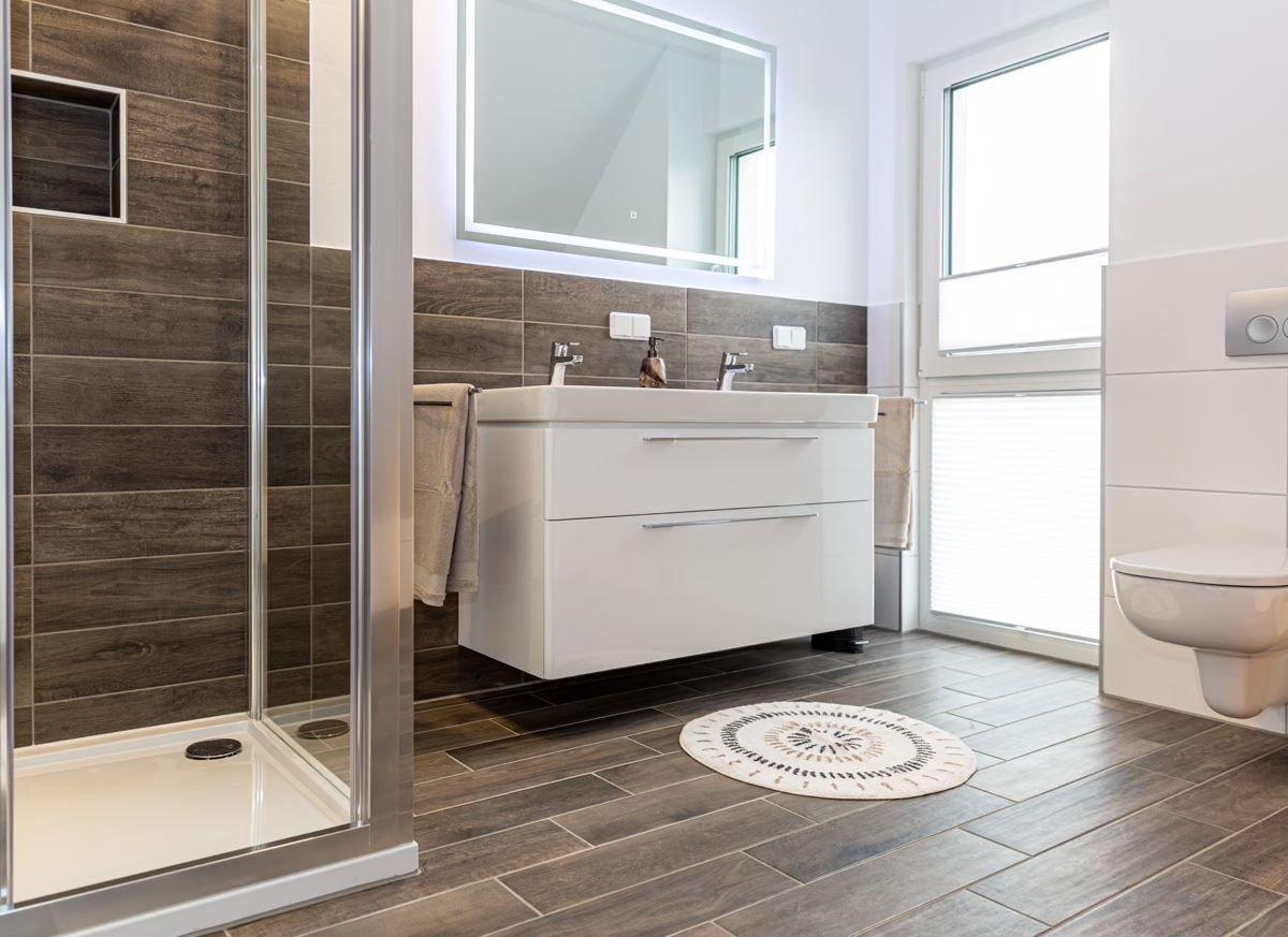 Badezimmer mit Dusche, Waschbecken und Toilette. Holzoptik und weißer Waschtisch.