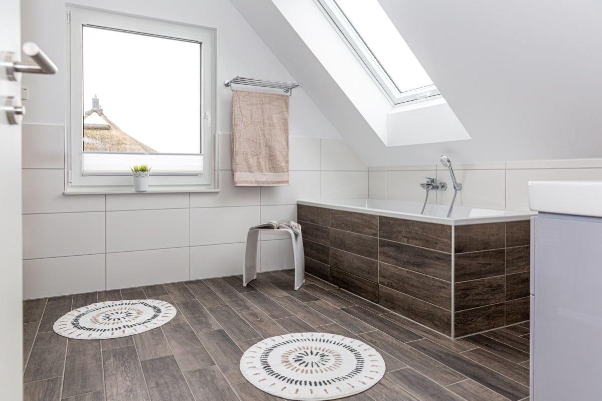 Badezimmer mit Dachfenster, Badewanne und zwei runden Teppichen auf Holzdielenboden.