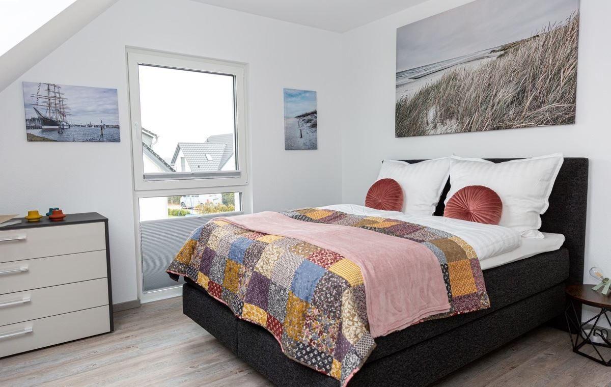Schlafzimmer mit Bett, Schrank und Fenster. Wandbilder zeigen Strand und Segelschiff.