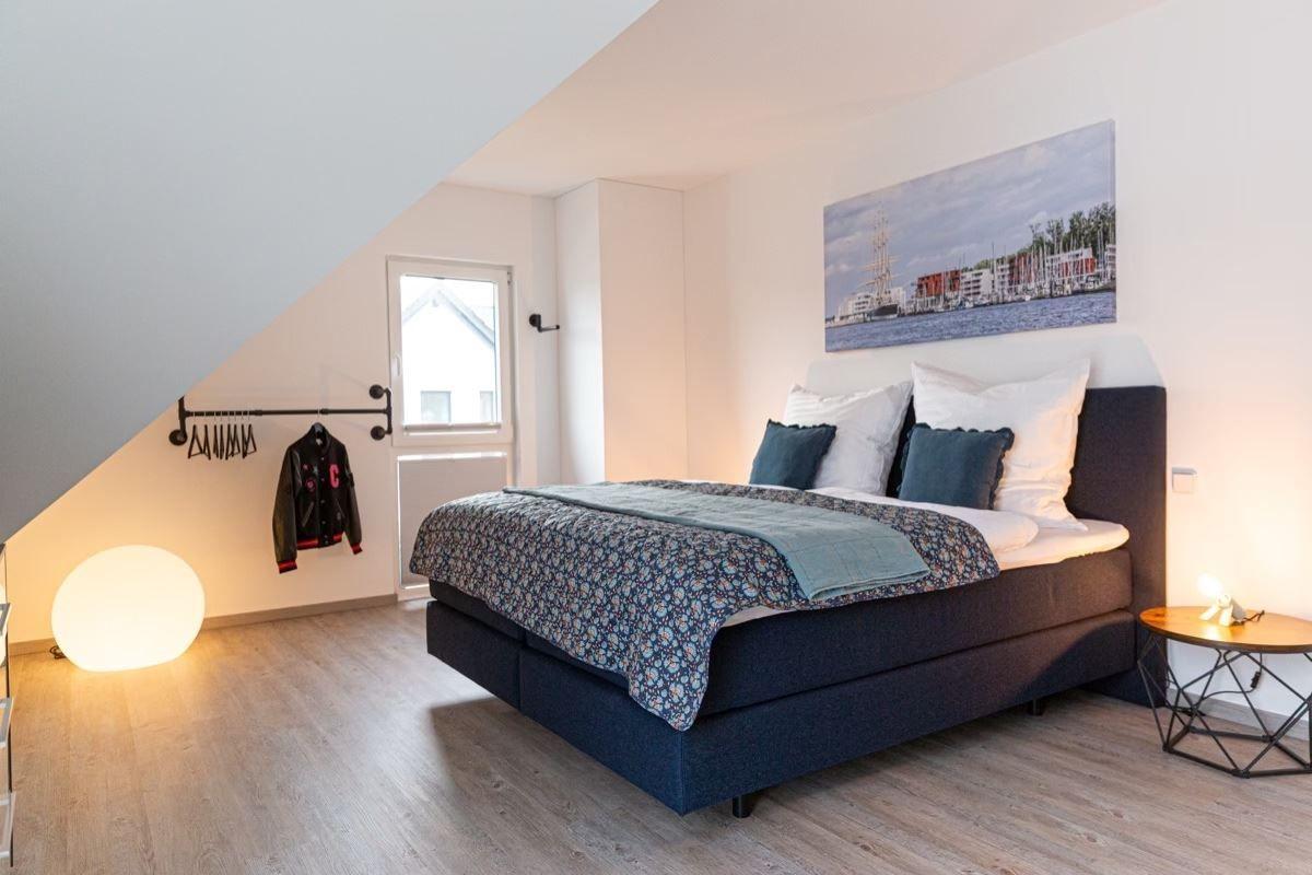 Schlafzimmer mit Dachschräge, Bett, Wandbild und Kleiderständer.