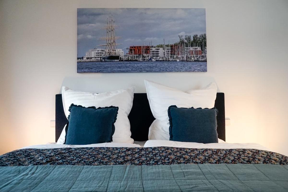 Doppelbett mit Kissen und Wandbild eines Hafens mit Segelschiffen.