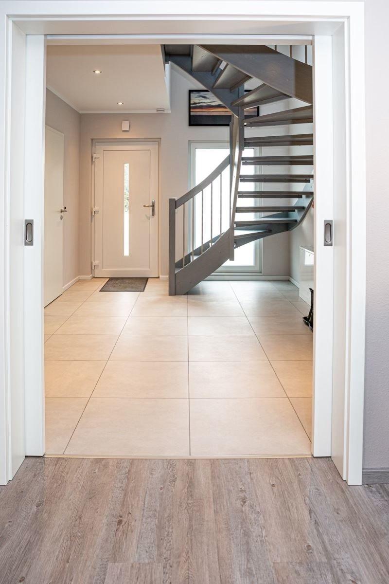 Haus-Eingang mit hellem Fliesenboden und schwarzem Wendeltreppe.