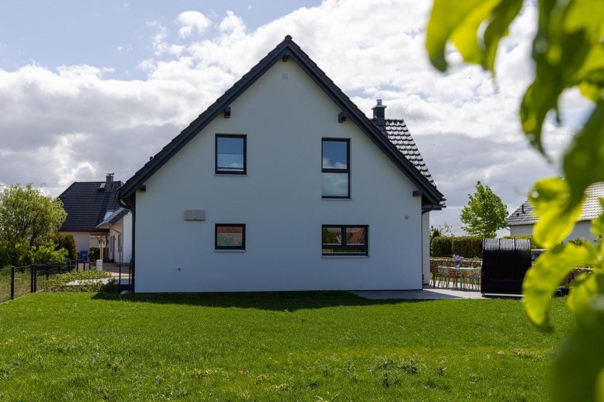 Modernes weißes Haus mit grünem Garten und Terrasse im Hintergrund.