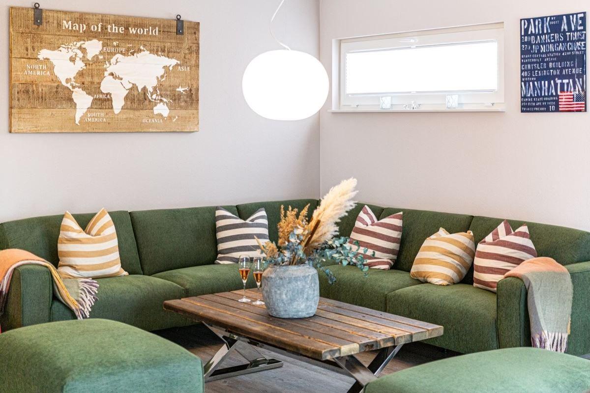 Grüner Sofa mit Kissen, Holztisch und Weltkarte an der Wand.