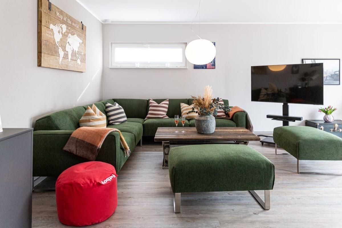 Ein Wohnzimmer mit grünem Sofa, Holztisch und Fernseher an der Wand.