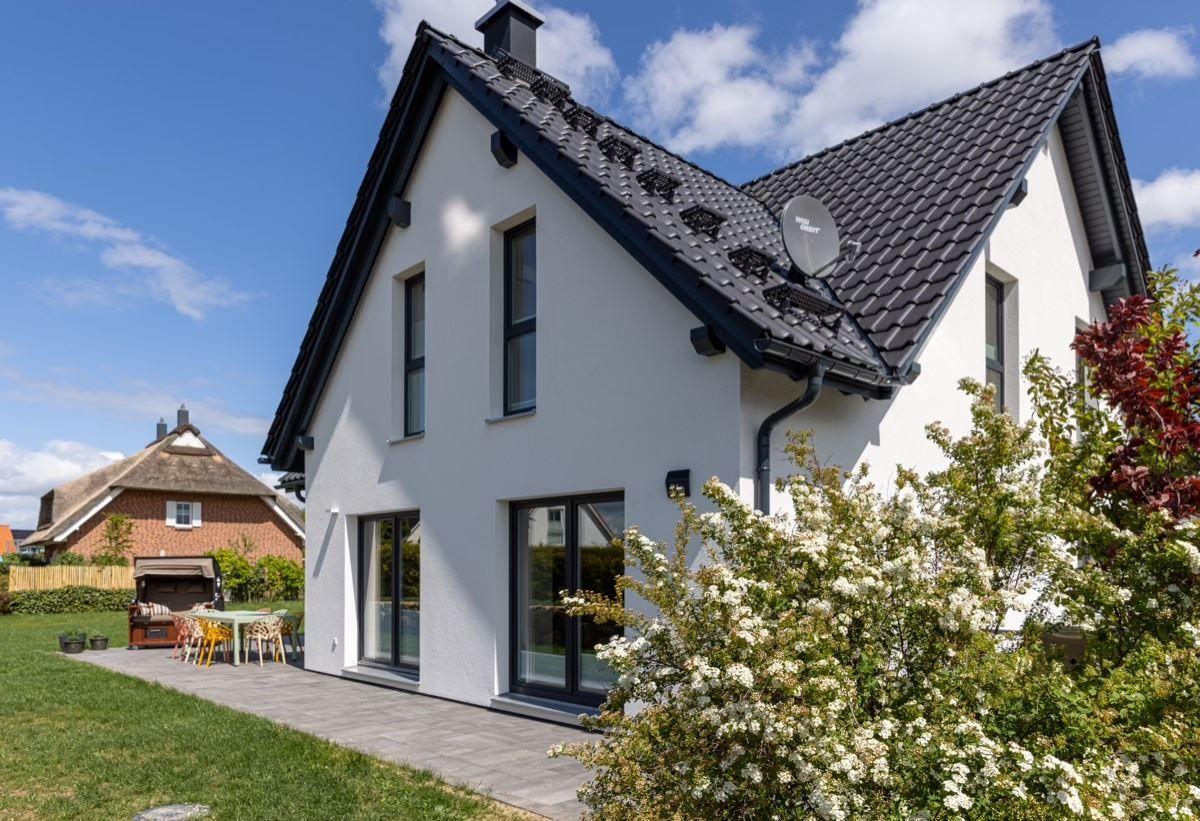 Moderne weiße Villa mit schwarzem Dach und Terrasse im Garten.