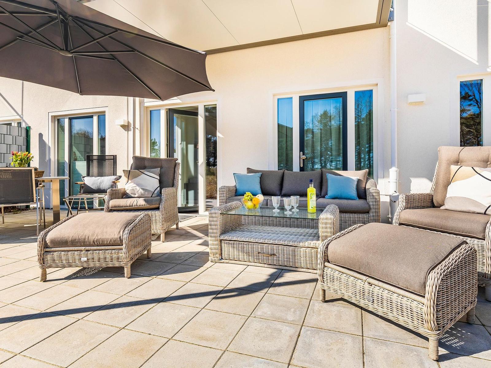 Terrasse mit Sitzgruppe, Sonnenschutz und Glas-Tisch. Hintergrund: Haus mit Fenstern.