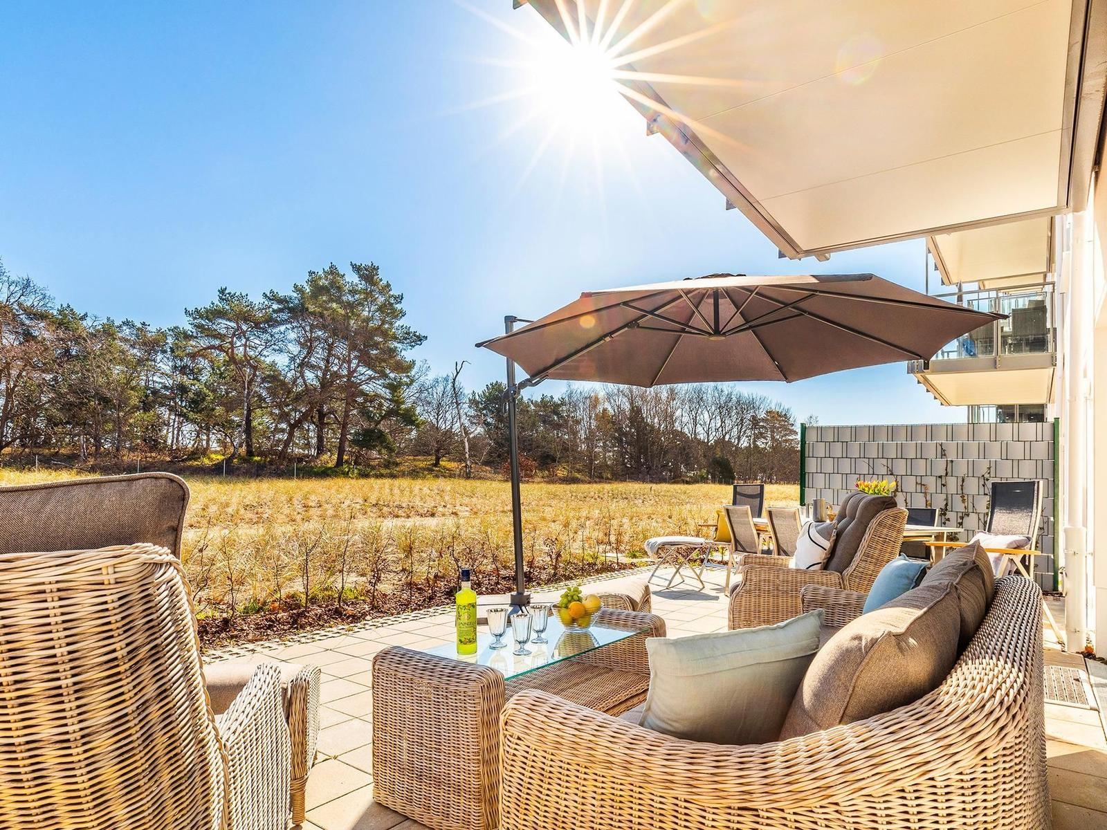 Terrasse mit Sitzgruppe, Sonnenschutz und Blick auf Wald.