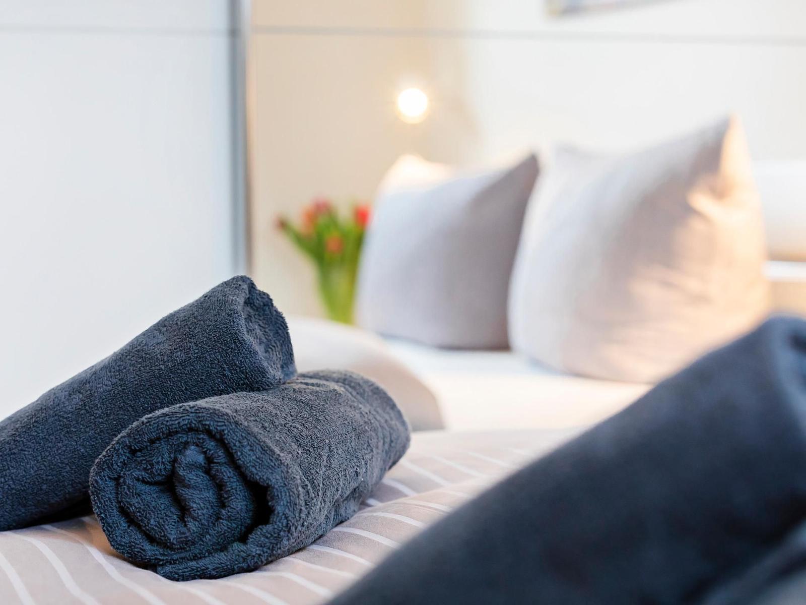Zwei gefaltete Handtücher liegen auf einem Bett mit Kissen und Blumen.
